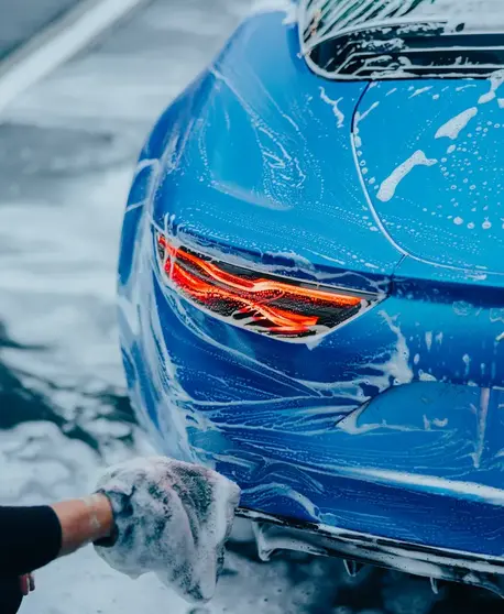 Mão a lavar um carro azul com uma esponja coberta de espuma